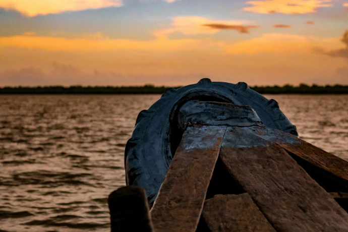 person in black gloves on brown wooden dock during sunset
